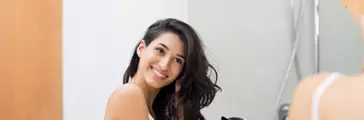 Beautiful girl using a hair dryer and smiling while looking at the mirror.