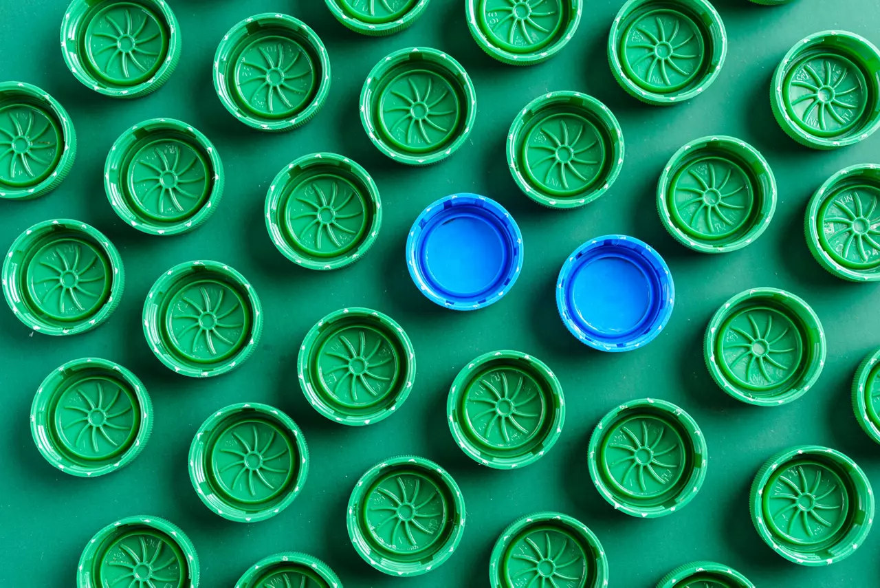 Plastic green caps from bottles and two blue caps, green caps have a design that looks like a sun.