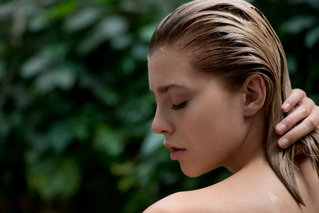 Eine schöne junge Frau trägt einen Balsam, ein Shampoo oder eine Spülung auf ihr geschädigtes Haar auf